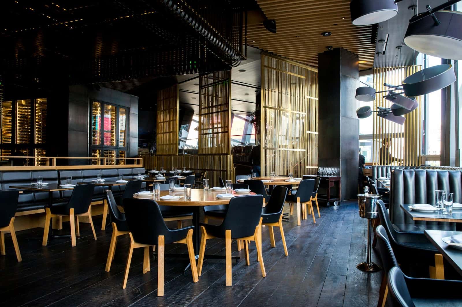 A modern restaurant dining room with set wooden tables and black chairs.